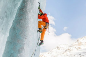 Cette photo prise par drone monte un alpiniste en train d'effectuer l'ascension d'une paroi entièrement glacée, à l'aide de pics à glace et de crampons.